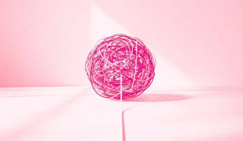 Bright pink ball of tangled string on a pale pink surface, with a single strand trailing forward into the foreground.