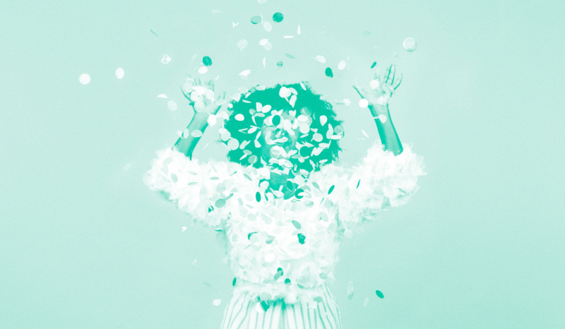 Person celebrating as confetti rains down, arms raised and face obscured by falling pieces in a monochrome teal-toned image.