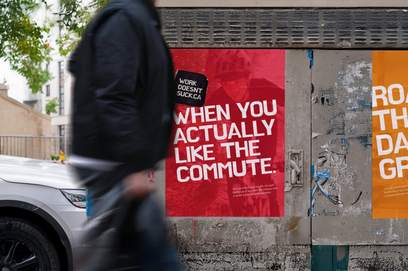Street poster reading “When you actually like the commute.” on a city wall, partially obscured by a passerby walking by.