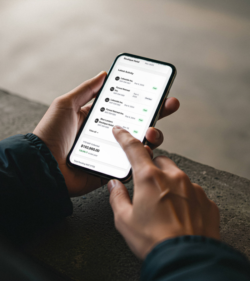 Close-up of a person holding a smartphone and scrolling through the Kingston MAT Tool mobile dashboard, viewing recent reporting activity and MAT totals.