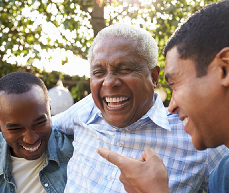 Three men outdoors laughing together, one pointing playfully as the group shares a light moment.
