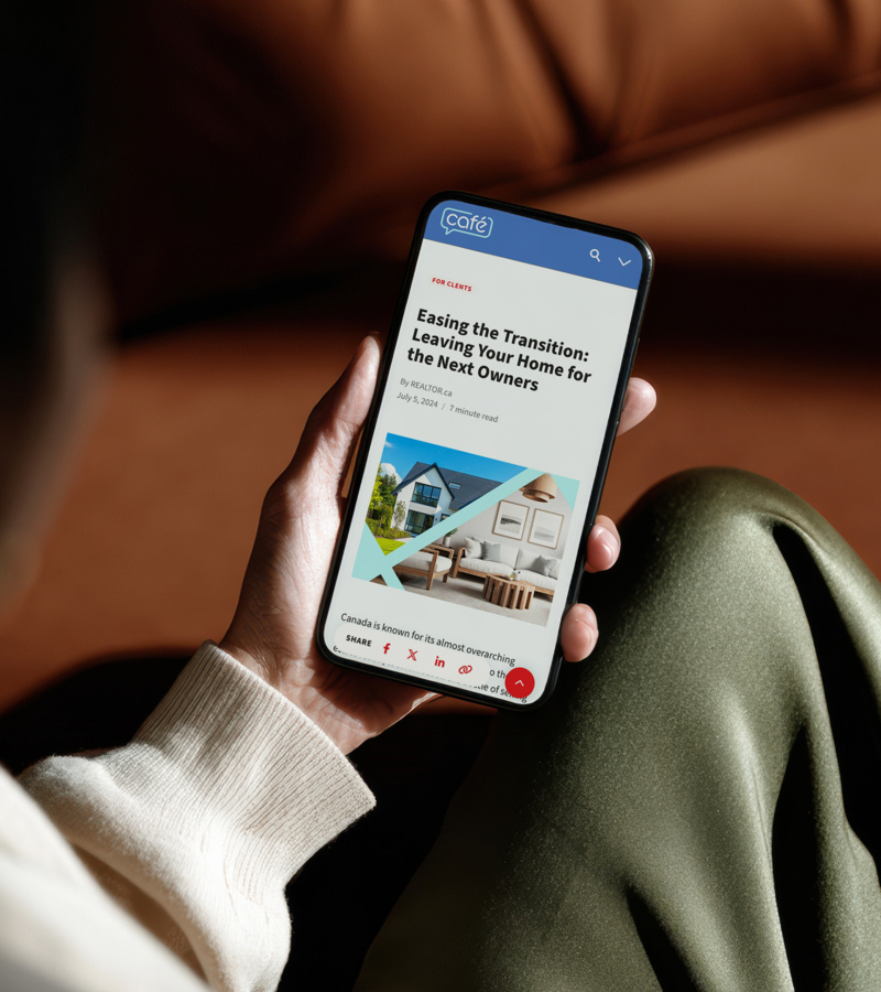 Person holding a smartphone while scrolling a CREA Café article titled ‘Easing the Transition: Leaving Your Home for the Next Owners,’ with the site’s blue header and geometric image layout visible on screen.