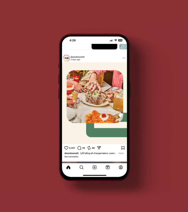 Phone displaying Instagram post of friends sharing a meal, with hands reaching for bread and drinks on the table.