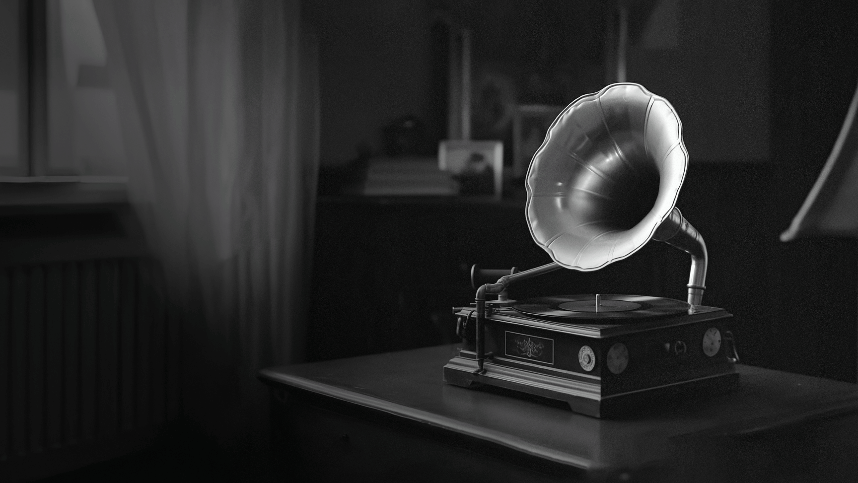 Black and white photo of a vintage gramophone on a wooden table by a window.