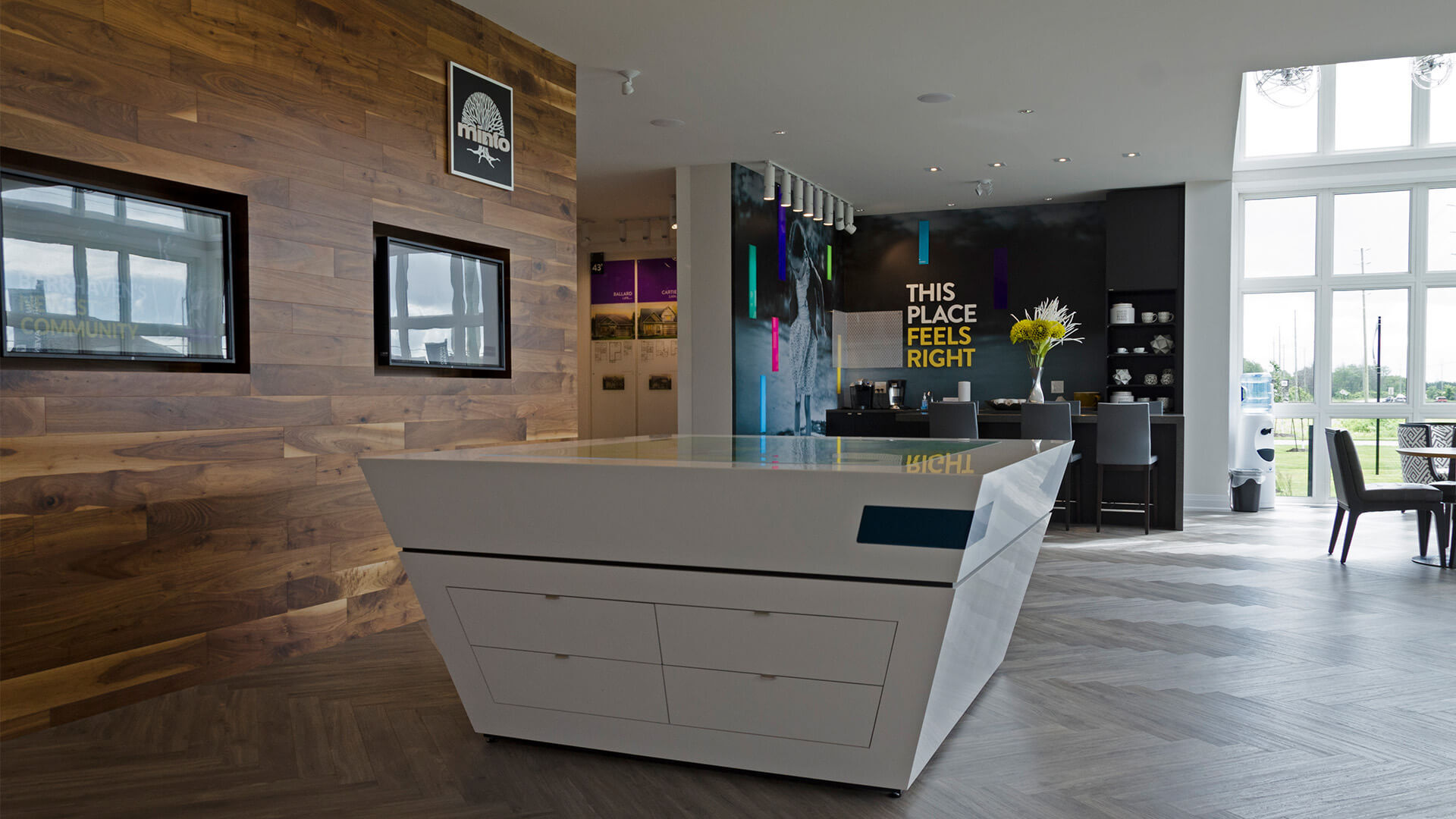 Interior of the Minto Quinns Point sales centre featuring a central display table, wood wall finishes, and the tagline “This place feels right.” in the background.