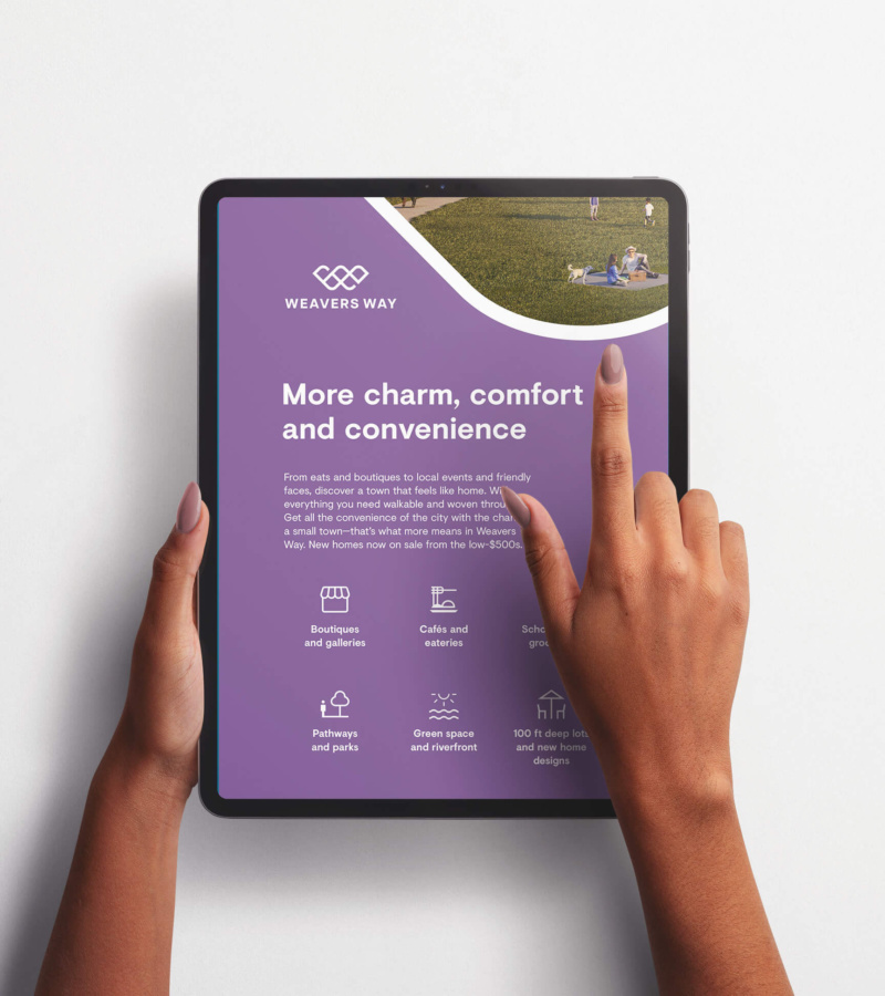 Hands holding a tablet displaying a Weavers Way digital ad promoting new homes with icons for community amenities.