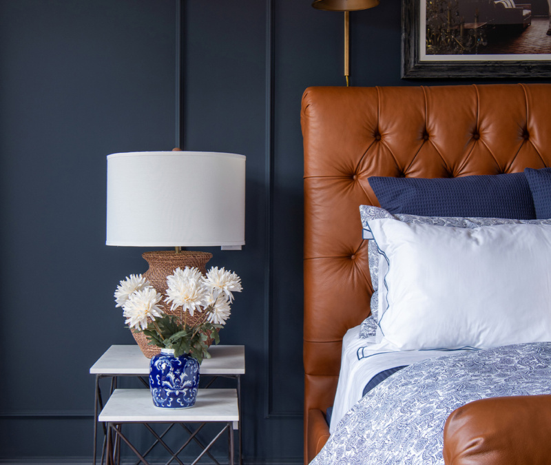 Bedroom with tufted leather headboard, navy wall, and floral bedside decor.