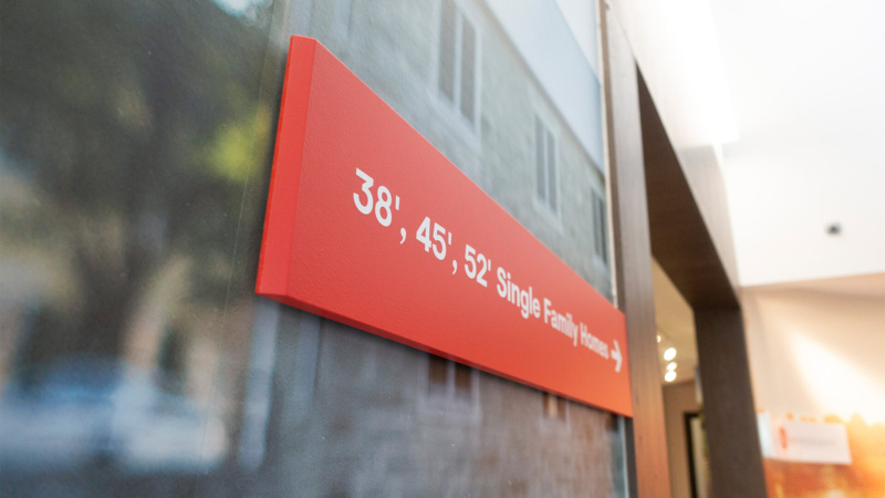 Close-up of a red wayfinding sign reading “38’, 45’, 52’ Single Family Homes this way” mounted on a wall inside the Minto Mahogany sales centre.