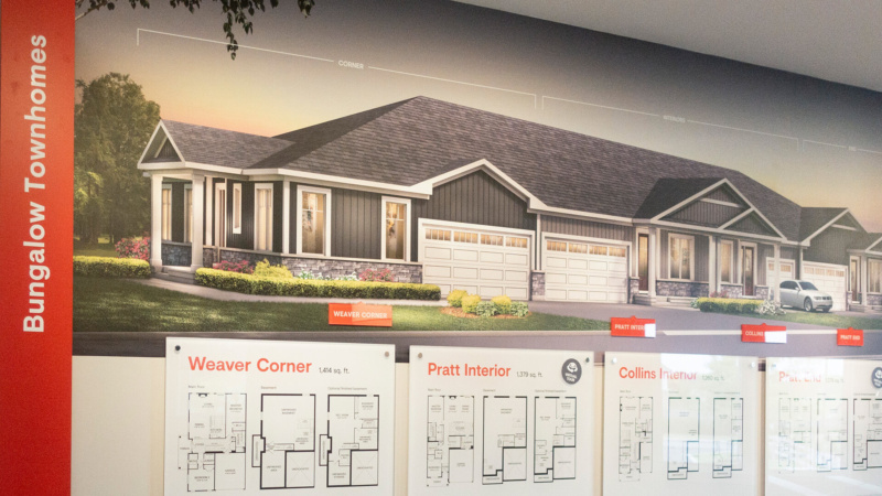 Interior of the Minto Mahogany sales centre showcasing a large wall mural of bungalow townhomes above detailed floor plan displays.