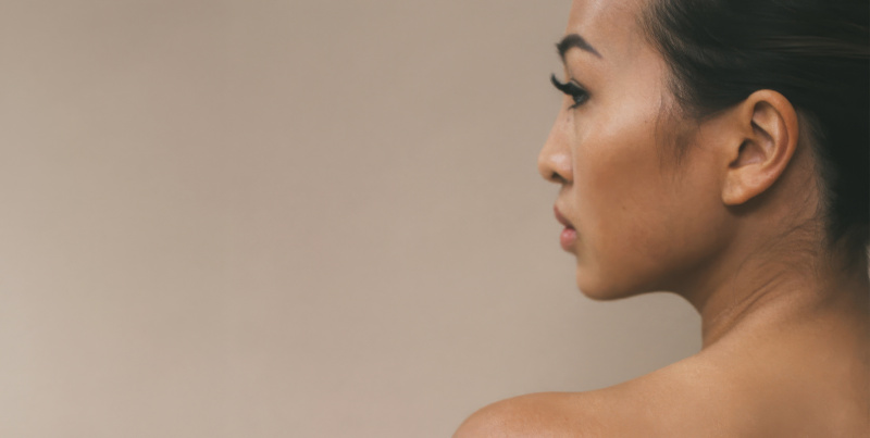 Side profile of a woman with smooth skin against a soft beige background.