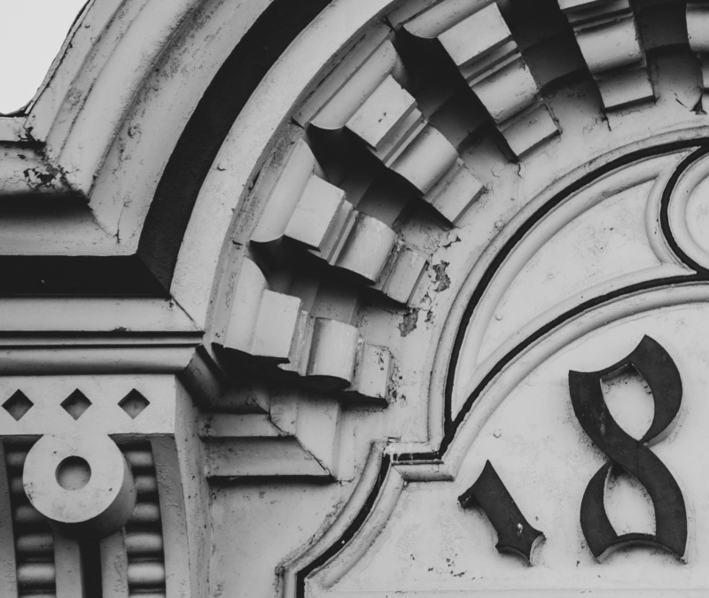 Close-up of historic building details with the number “1878” in black-and-white, showing ornate stonework and weathered texture.