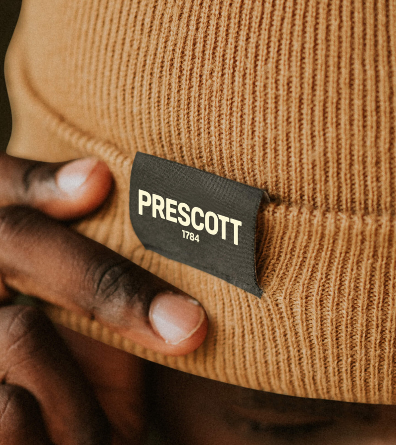 Close-up of a knit hat with a black label reading “Prescott 1784”.
