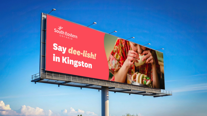 Large billboard reading “Say dee-lish! in Kingston” beside an image of a woman eating Viatnamese bao,