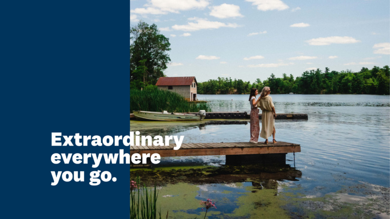 Two women standing on a dock by a lake with text reading “Extraordinary everywhere you go.”