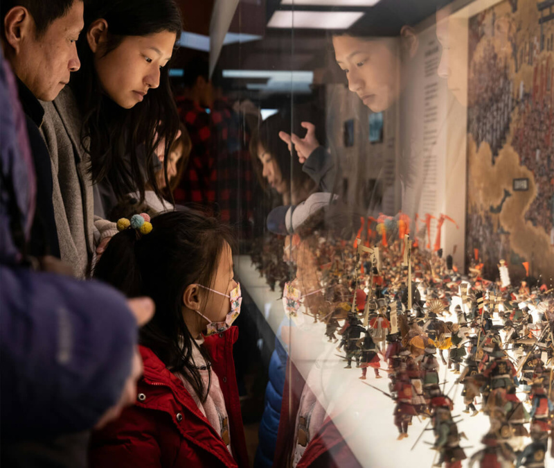 Family admiring miniature battle figures in a glass museum display under warm lighting.