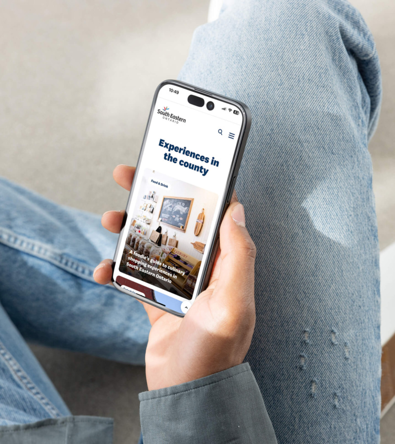 Person holding a phone showing the South Eastern Ontario website page “Experiences in the county.”